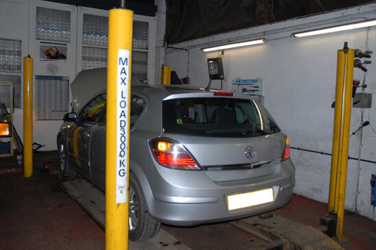 Silver hatchback on the MOT testing bay between yellow lift posts